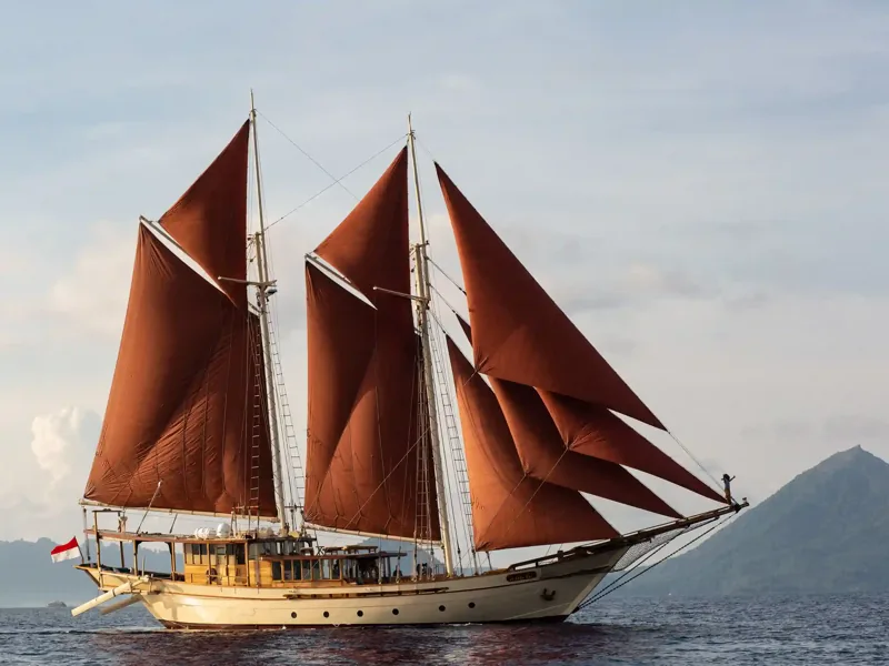 Phinisi with red sails cruising past the islands of Komodo