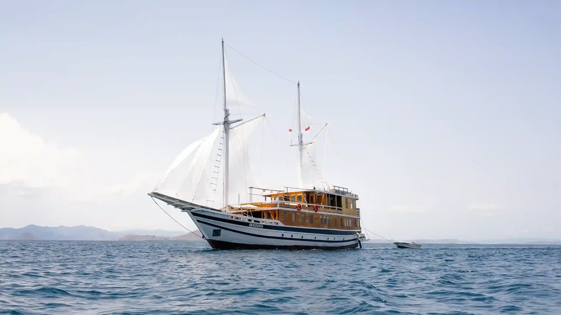 A phinisi under full sail off the hills of Komodo National Park
